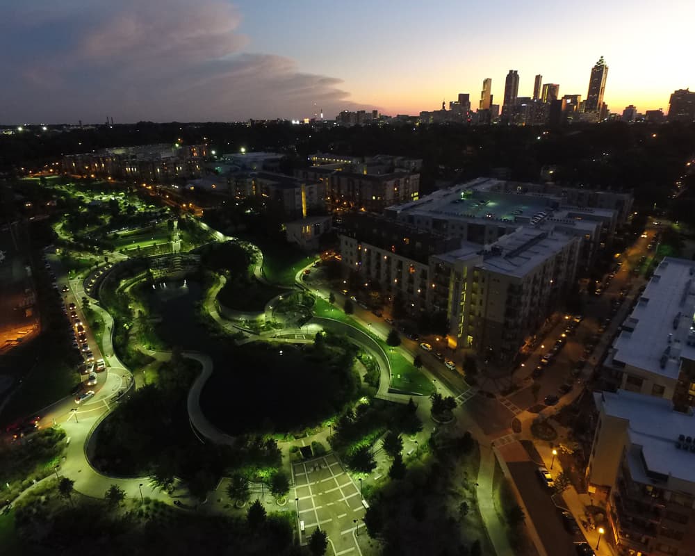 Evening aerial view of a city with a winding lit park, ponds, and surrounding apartment buildings