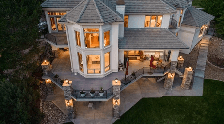 A modern multi-story house with illuminated windows, a wraparound porch, and stone columns