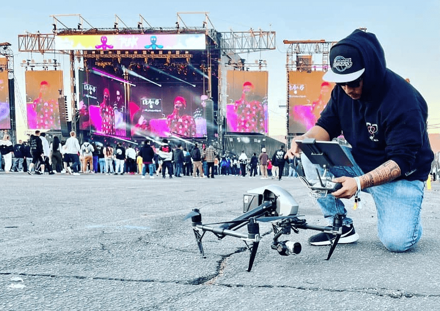 Drone on the ground with a kneeling operator holding a tablet near a concert stage and screens