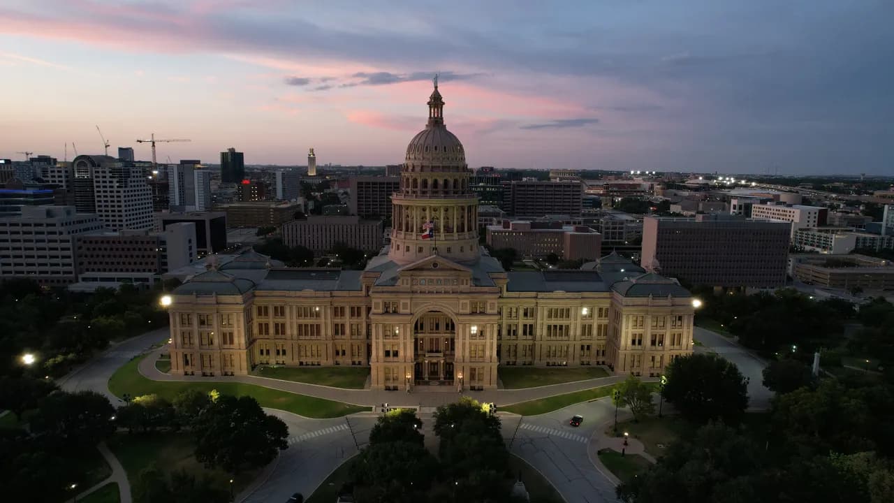 Aerial view of a domed capitol building at dusk with surrounding city and cranes