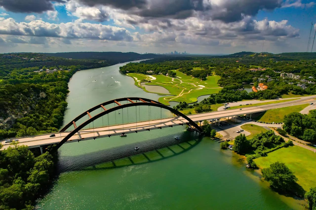 Aerial view of a large red arch bridge crossing a winding river, with a golf course and trees on the banks