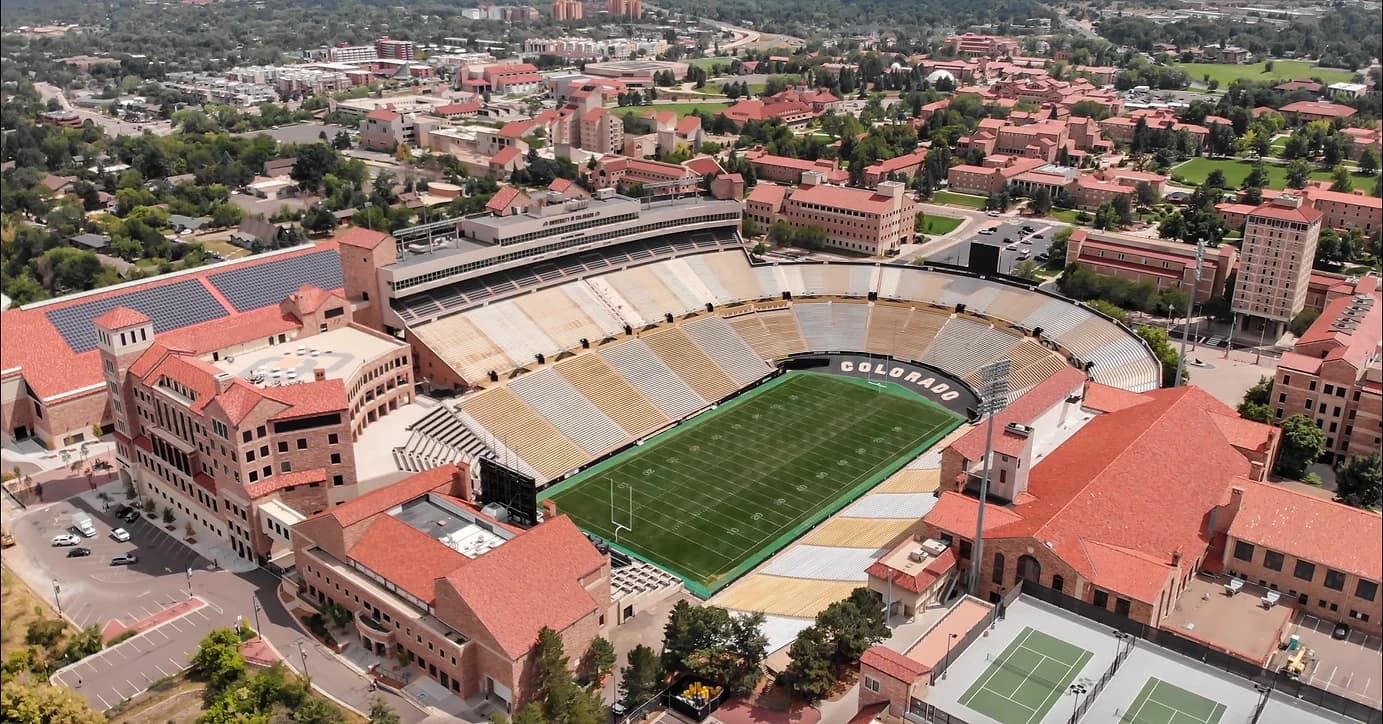 Aerial view of a football stadium with green field and Colorado seating, surrounded by red-roofed buildings