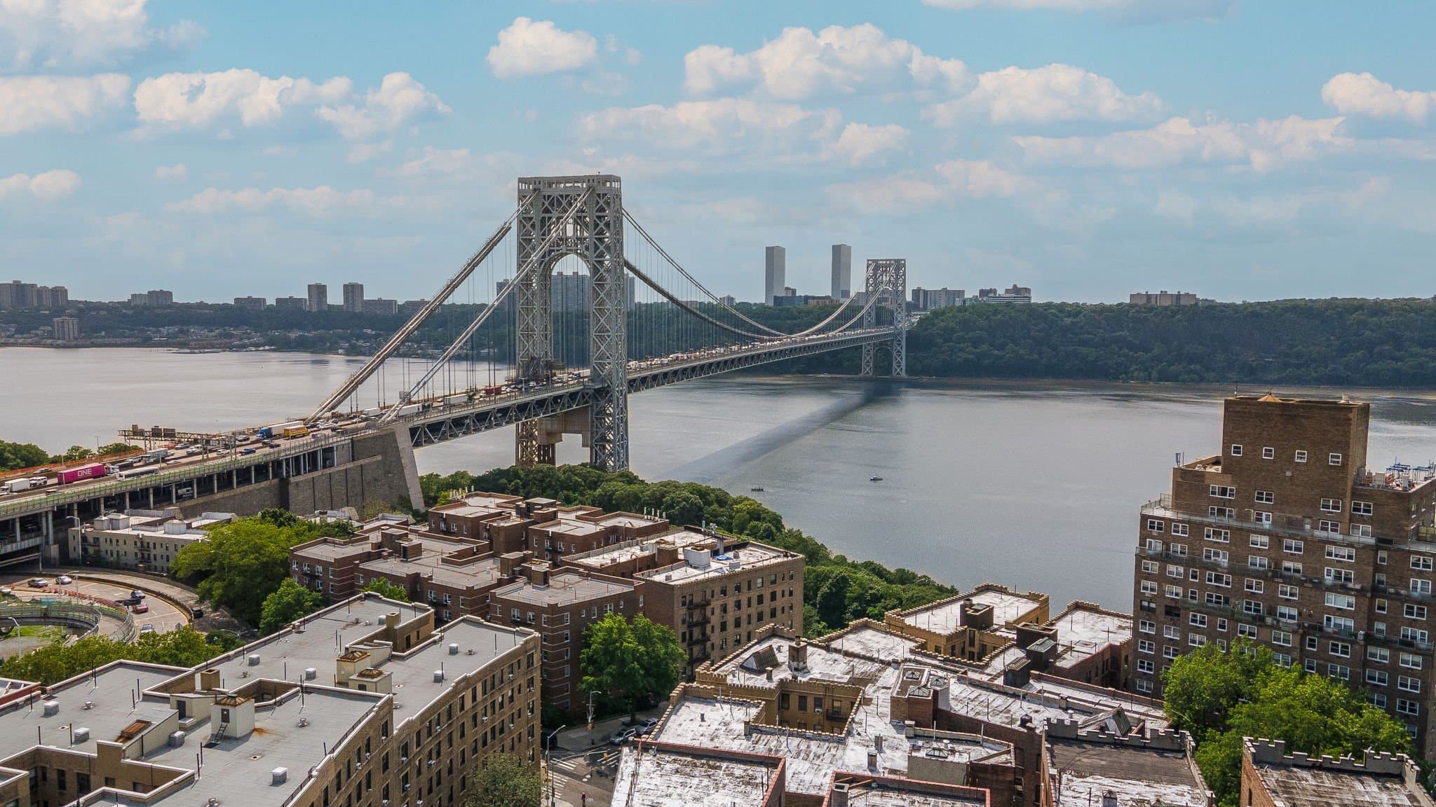 Two-tower suspension bridge crosses a river with a city skyline in the background