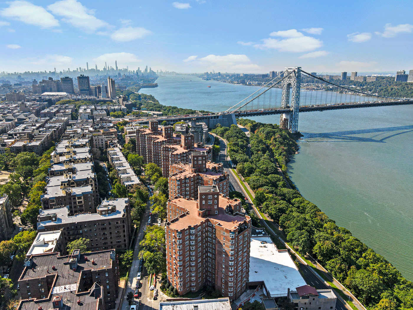 Aerial view of a suspension bridge over a wide river with apartment blocks along streets and distant skyline