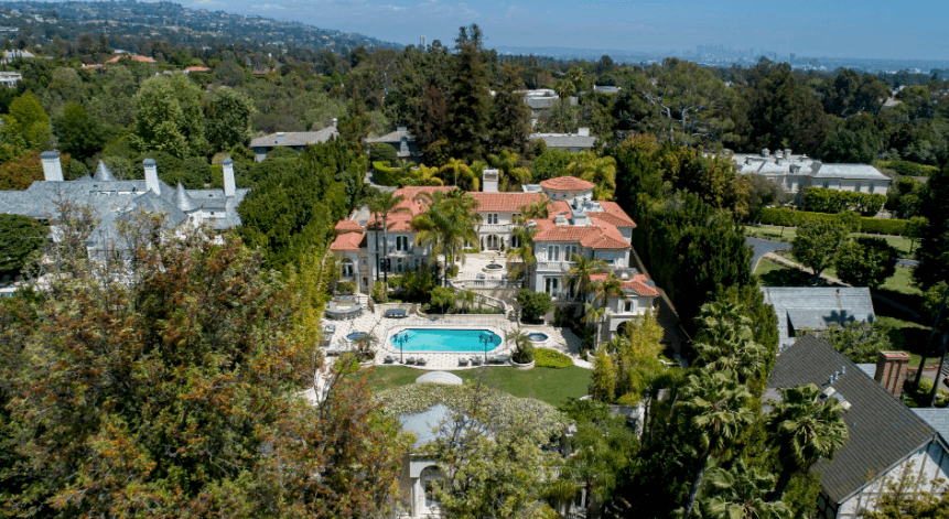 Aerial view of a large villa estate with red-tiled roofs, a central pool, palm trees, and lush landscaping