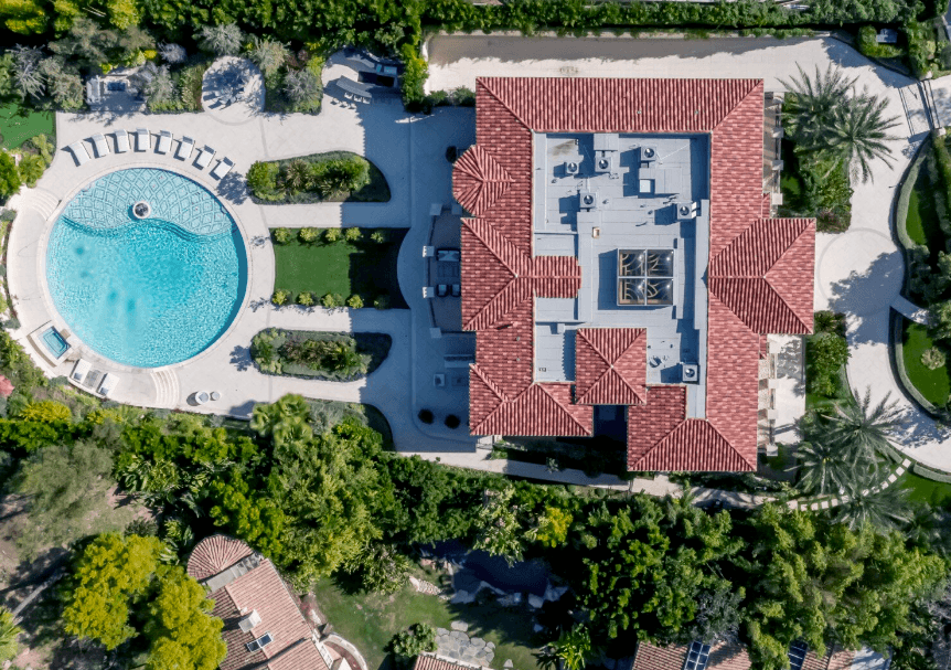 Aerial view of a villa with red tile roof, circular pool, and manicured landscaping