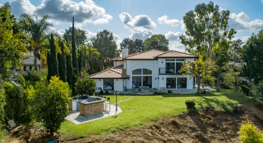 Two-story white house with red tile roof and large arched windows, balcony, and a circular stone seating area